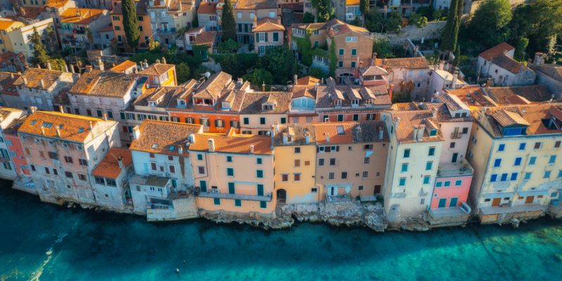 Aerial view of beautiful old houses with orange roofs at sunset in summer in Rovinj, Croatia. Top view of colorful architecture in old city and sea coast. Historical centre, buildings on the water